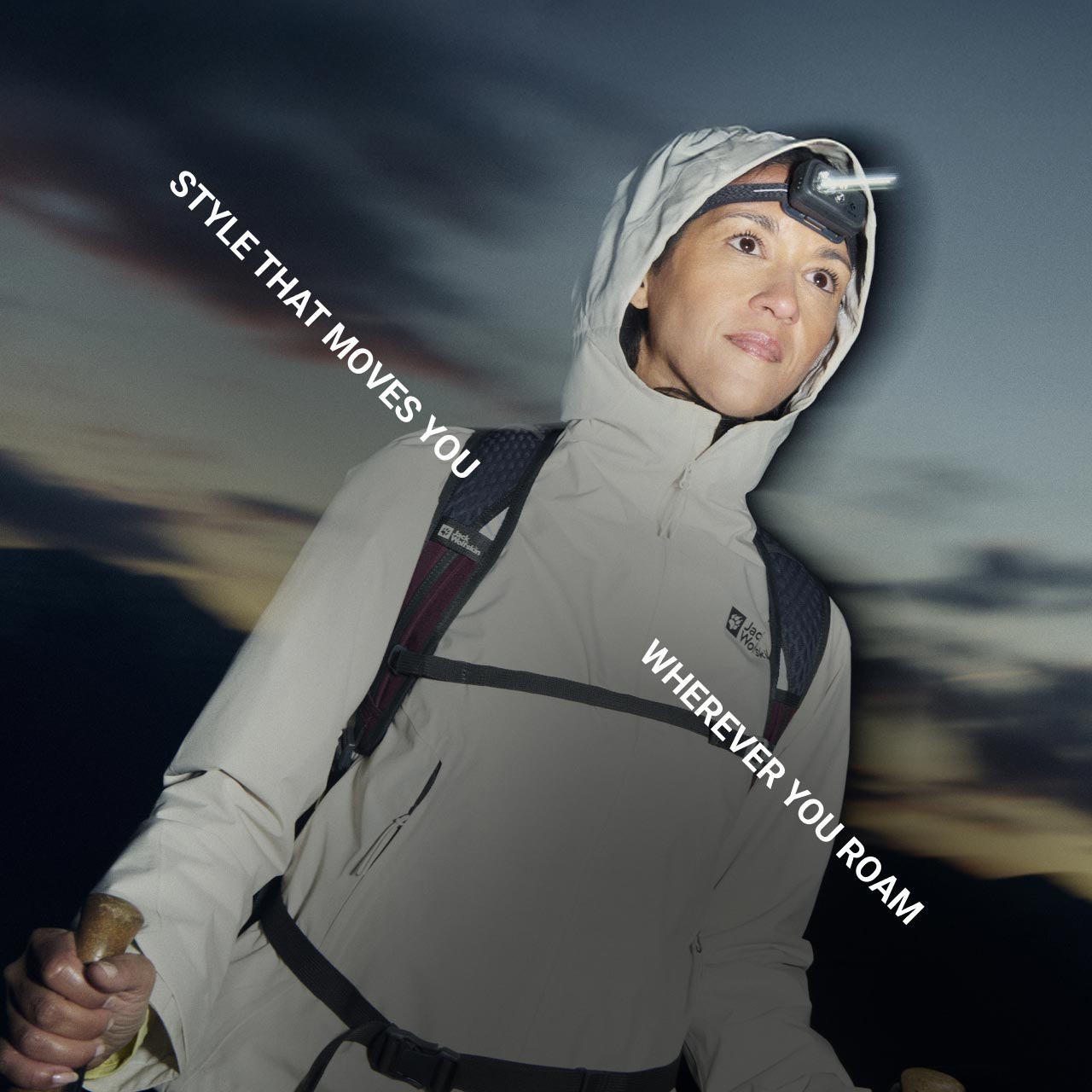 A person in outdoor gear with a headlamp gazes forward, holding trekking poles in the mountain twilight. Overlayed text reads, "Style that moves you wherever you roam"