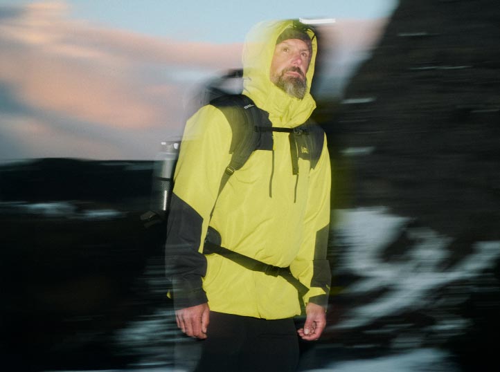 Man in a bright yellow jacket and backpack hiking at dusk, motion blur adds a dynamic feel.