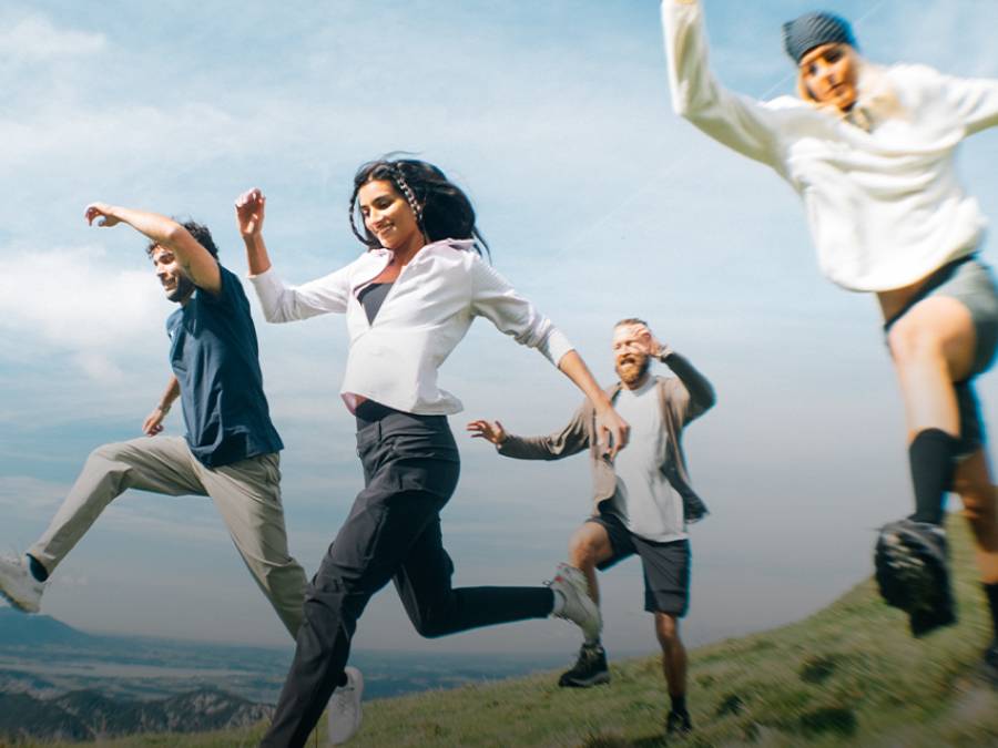 Four people in summer hiking gear run across a field