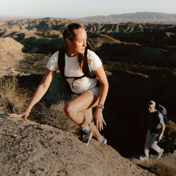 A couple in summery hiking clothes climbing up a rock